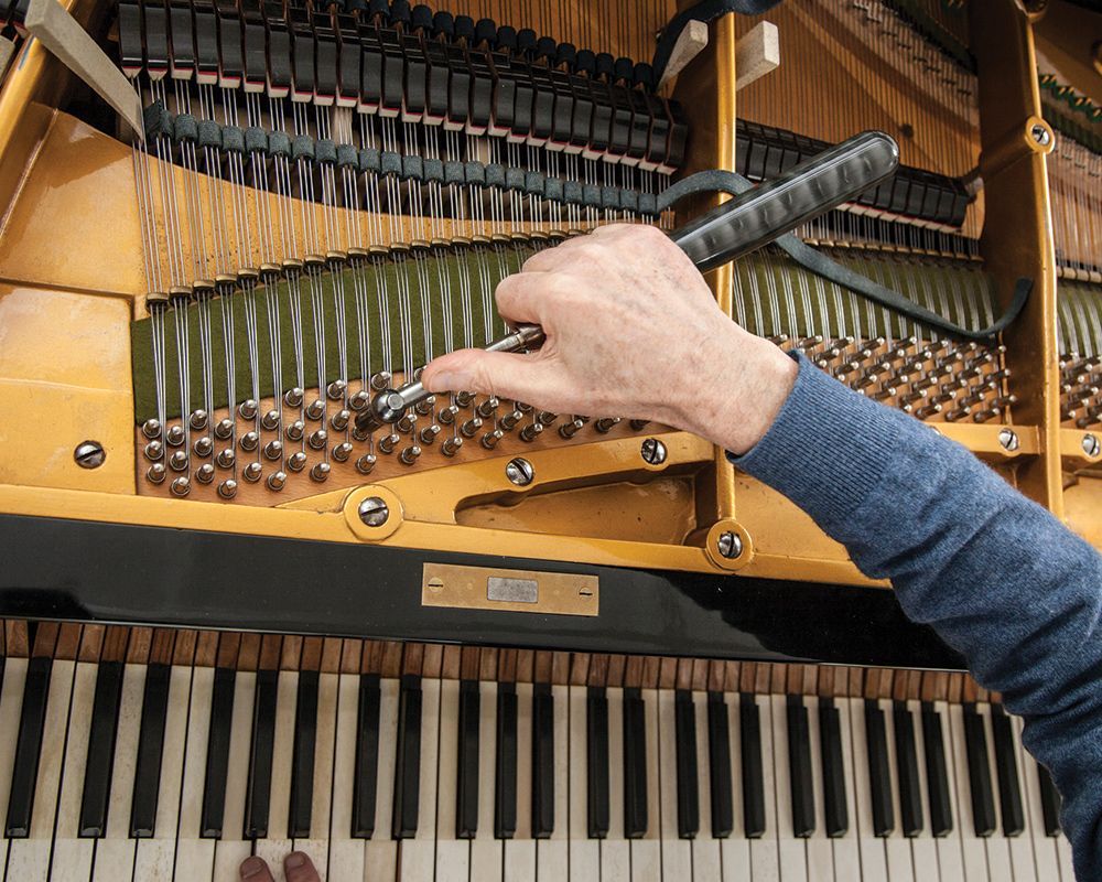 Closeup of piano tuner working on a grand piano with specialized tools. Closeup of piano tuner working on a grand piano with specialized tools.