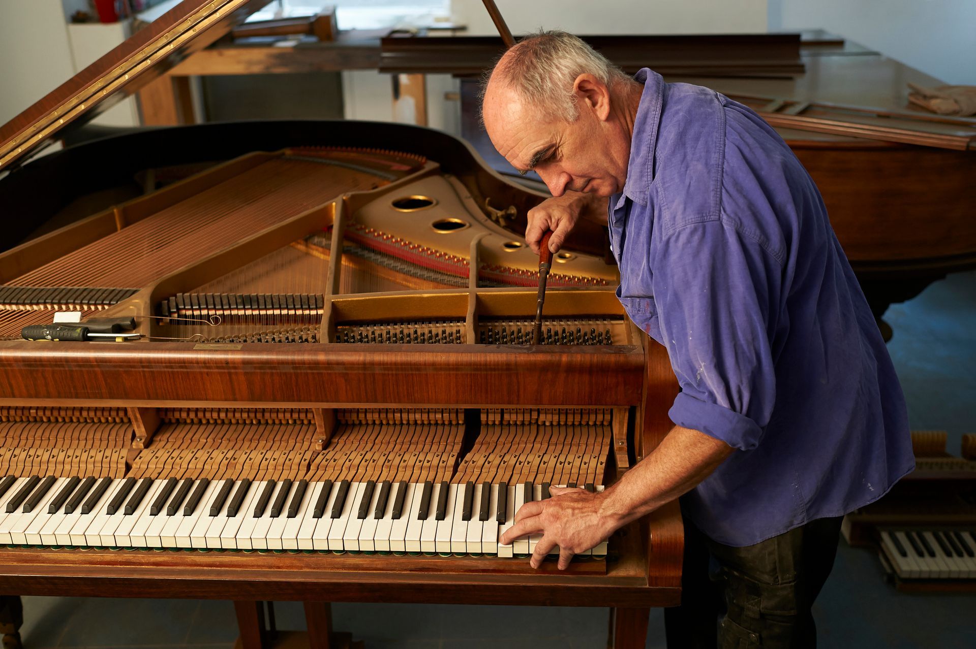 A man repairing a grand piano in a studio, performing expert piano repair with precision.