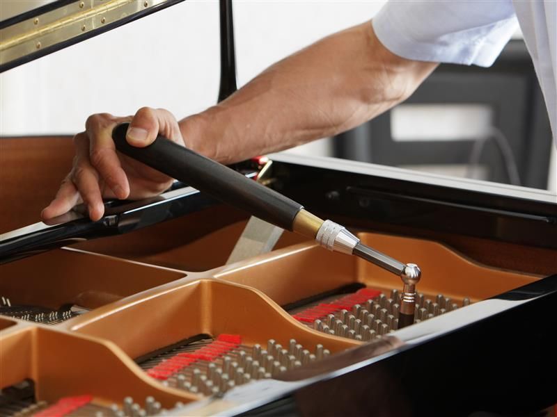 A man is working on a piano with a vacuum cleaner