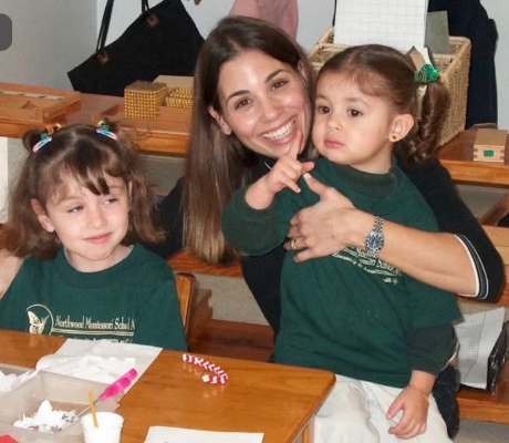 Three people in matching green shirts smiling at a classroom table with craft supplies
