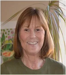 Smiling woman indoors in an olive green shirt, with a plant in the background
