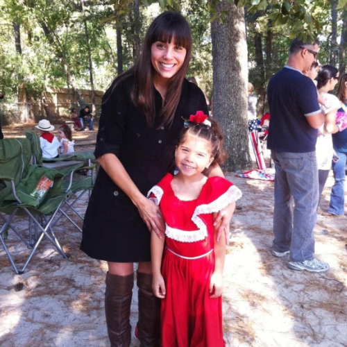 Two people smiling outdoors, one in a black dress and one in a red costume.