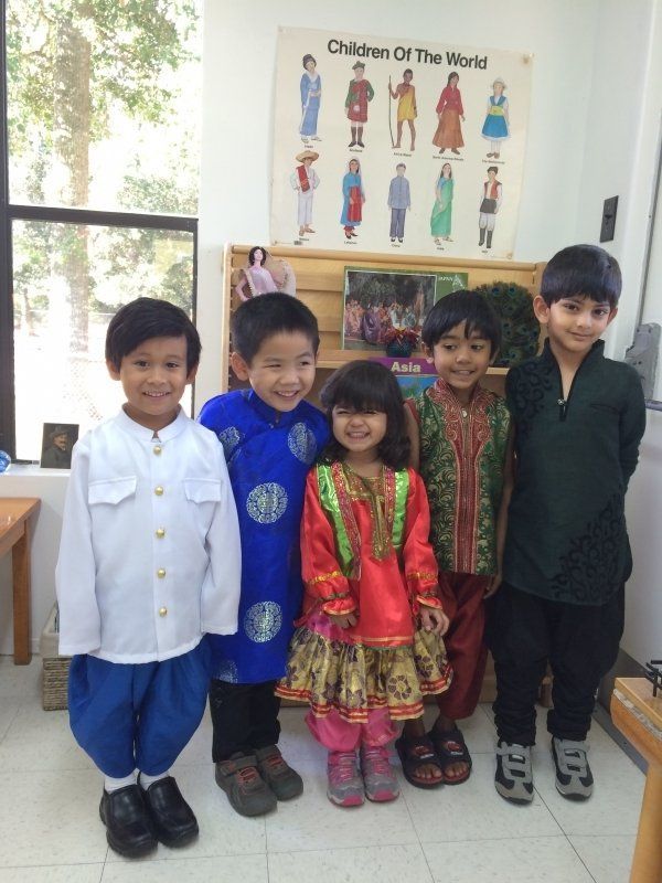 Five children in various traditional clothing, smiling, pose in a classroom setting with a 