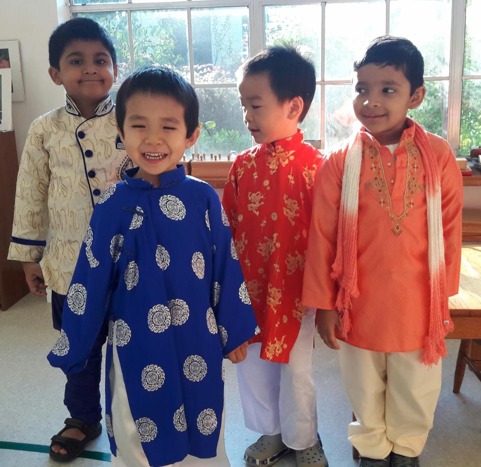 Four Montessori children smiling, wearing traditional clothing indoors near a window.