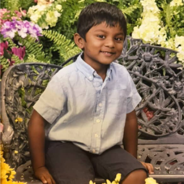 Smiling child in a light blue shirt sitting on an ornate bench with flowers behind him