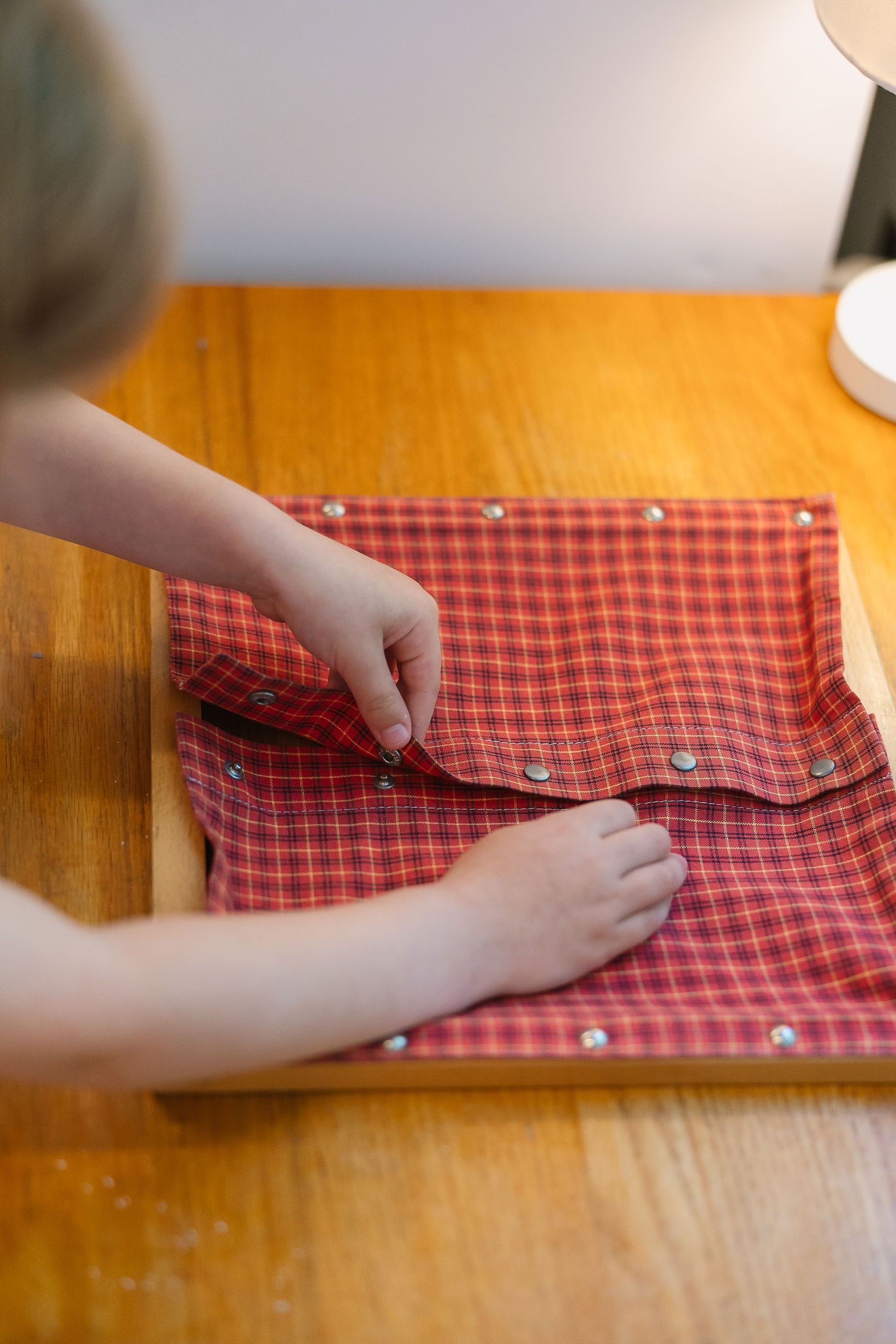 Hands opening red checkered fabric dressing frame on a wooden table