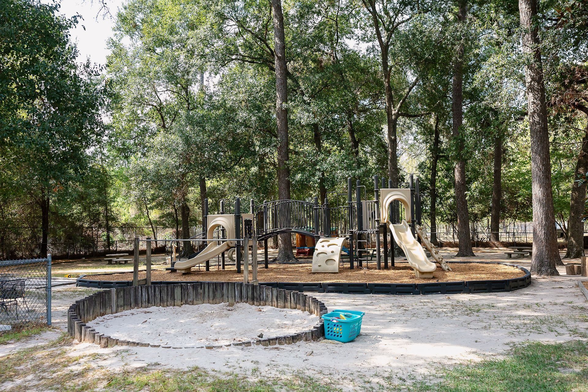 Playground at Northwood Montessori School with wooden structures, slides, sandbox, surrounded by trees.