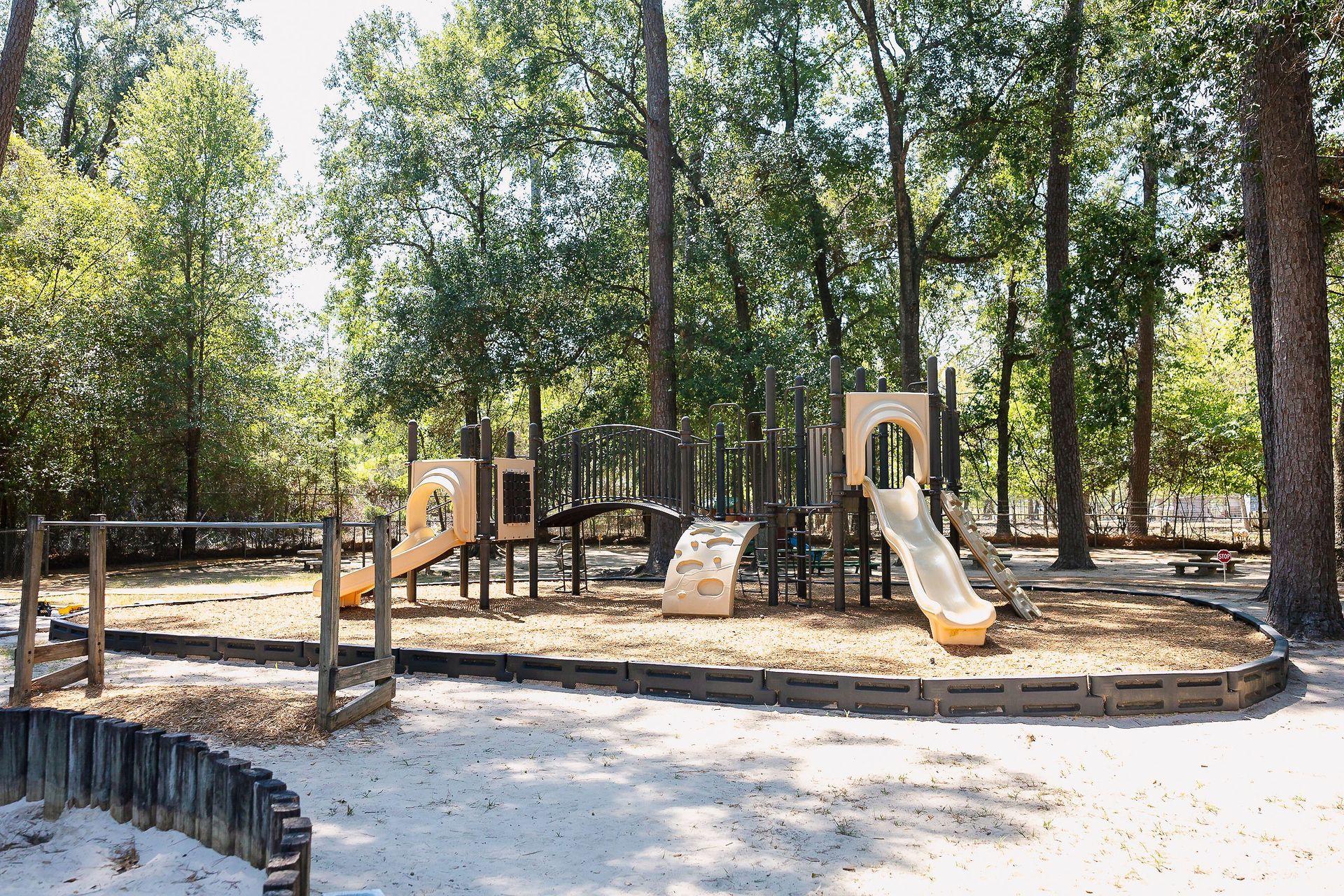 Playground at Northwood Montessori School with wooden structures, slide, and sand, surrounded by trees.
