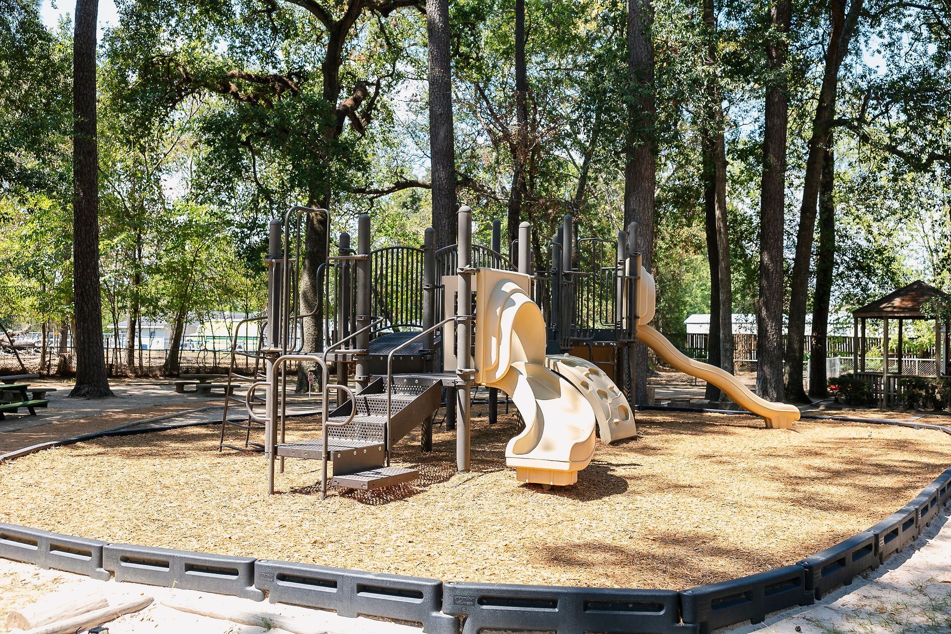 Playground at Northwood Montessori School with wood chip ground cover, slides, and climbing structures surrounded by trees.