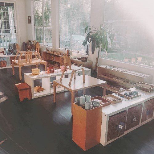 Montessori classroom with child-sized furniture and learning materials. Bright, airy space with large windows.