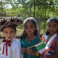 Three Montessori children in cultural outfits holding flags, outside.