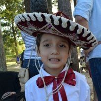 Montessori Boy wearing a sombrero and bow tie outdoors, smiling.