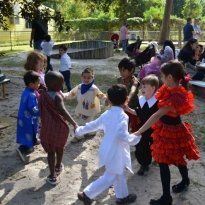 Montessori Children holding hands in a circle, smiling, in a sandy outdoor area.