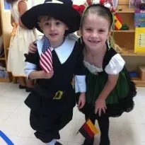 Two Montessori children in costumes pose together, one holding a flag.