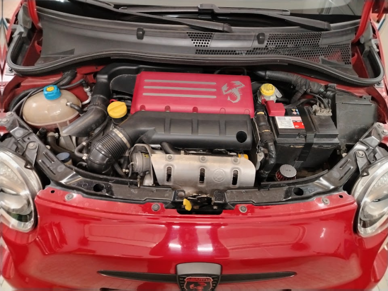 Vano motore di un'auto rossa con cofano aperto, che mostra una copertura del motore rossa e i componenti visibili.