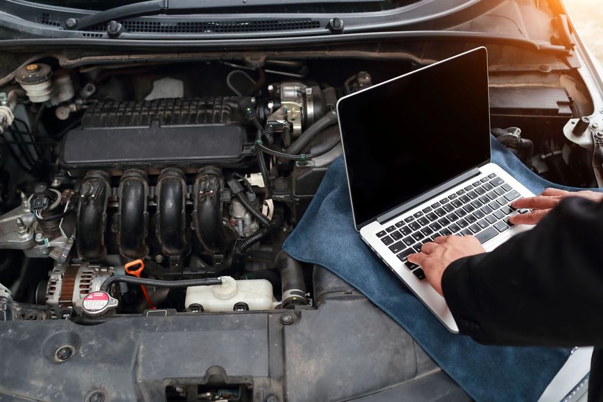 Un meccanico utilizza un computer portatile per diagnosticare un problema al motore di un'auto con il cofano aperto.