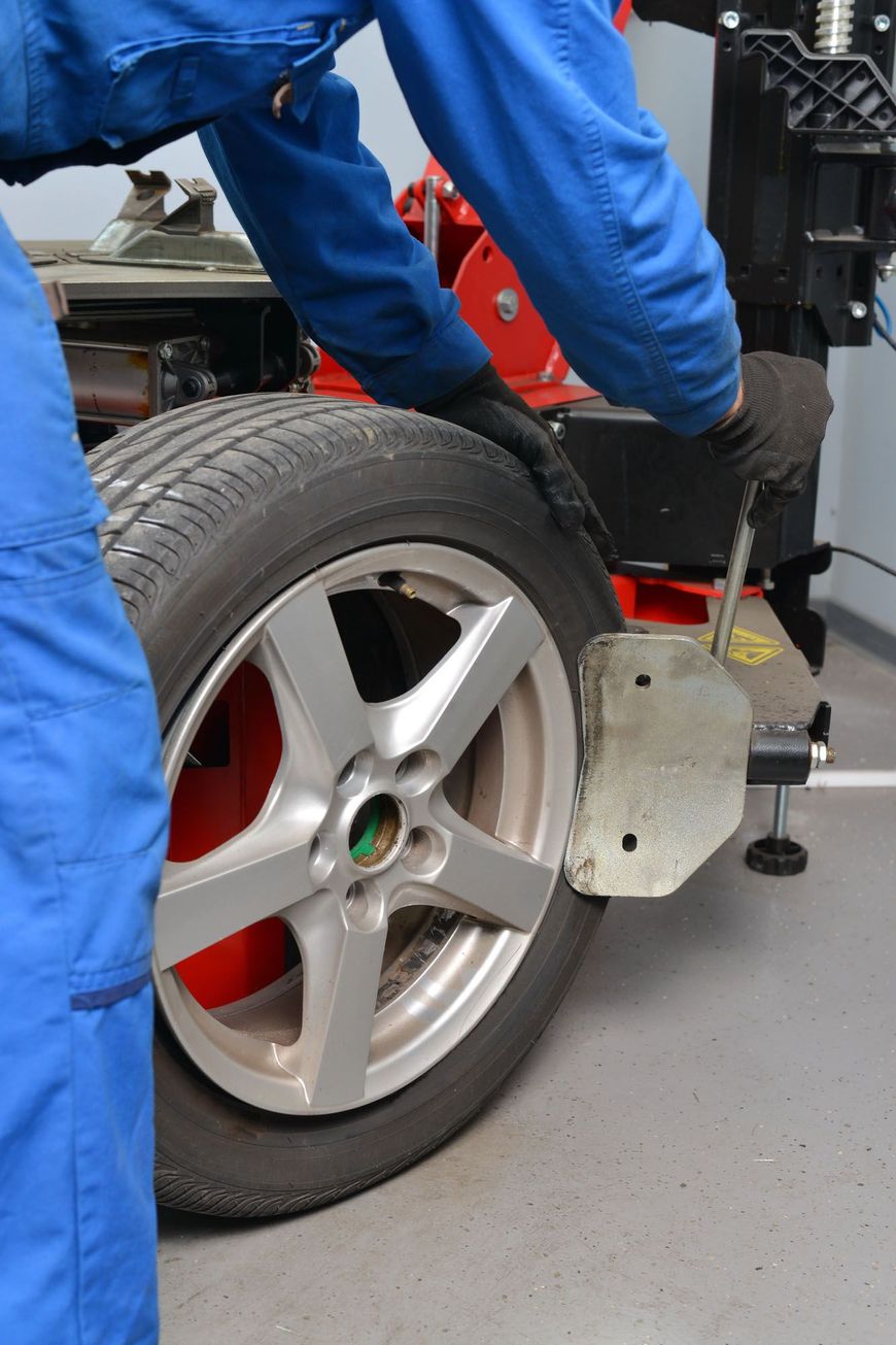 Un meccanico controlla l'allineamento delle ruote di un'auto con una macchina per l'allineamento rossa in un'officina.