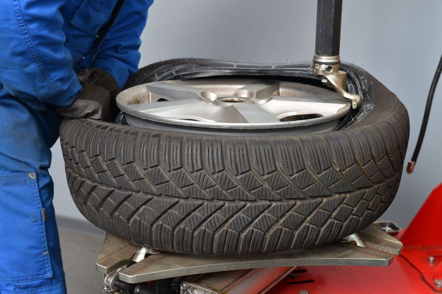 Pneumatico per auto montato su una macchina equilibratrice, con un meccanico in tuta blu nelle vicinanze.