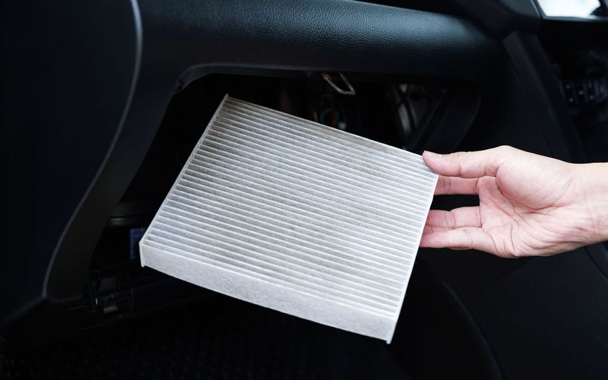 Sostituzione manuale di un filtro dell'aria abitacolo rettangolare nel vano del cruscotto dell'auto.