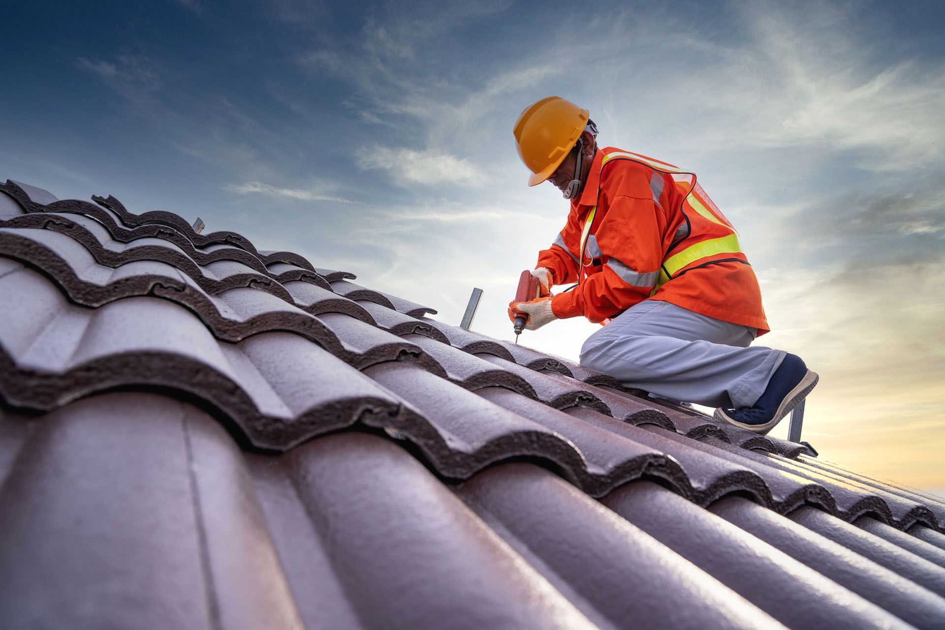 A residential roofing contractor, equipped with safety gear, is working on installing a roof.