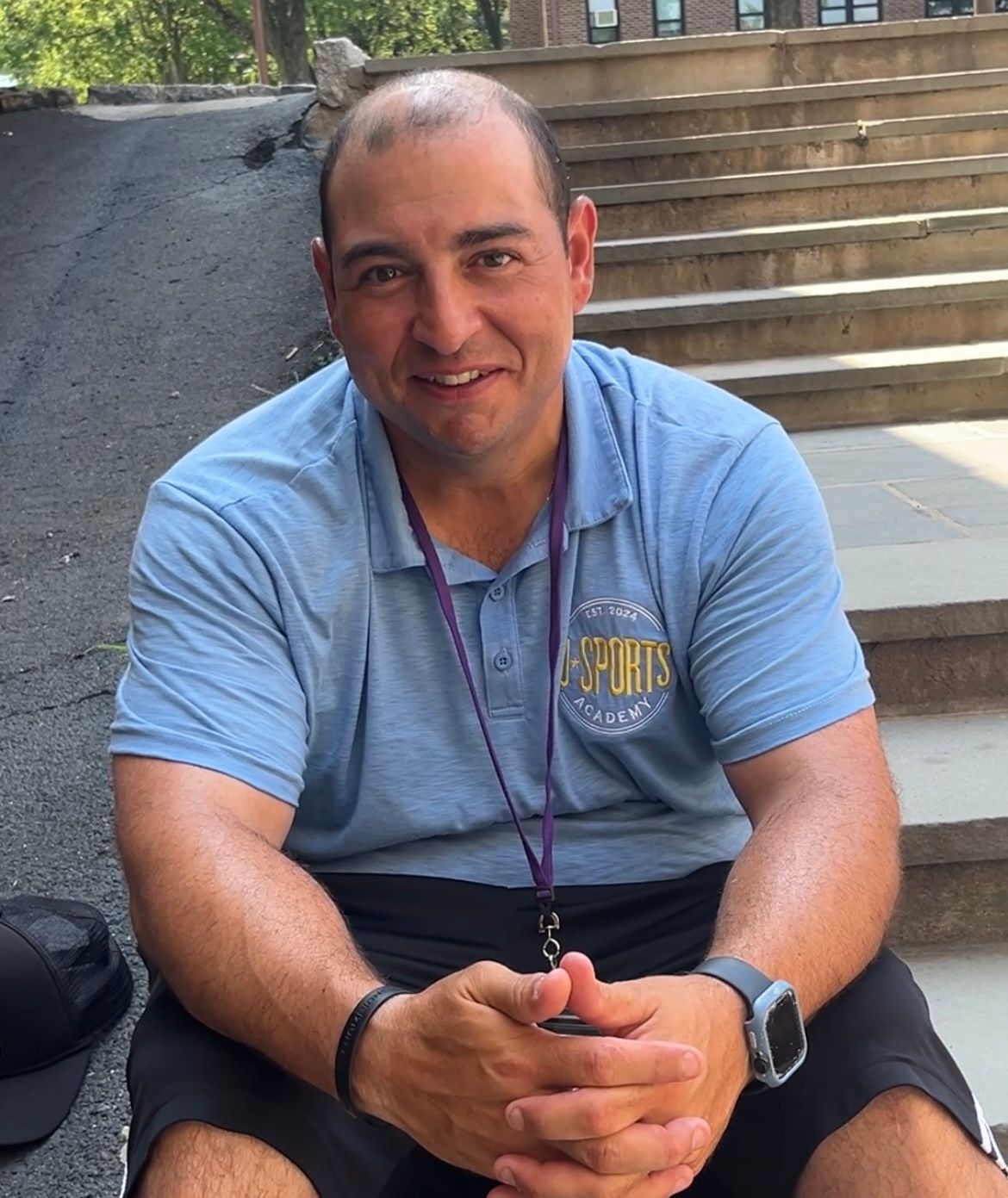 A man wearing a sports shirt is sitting on the ground