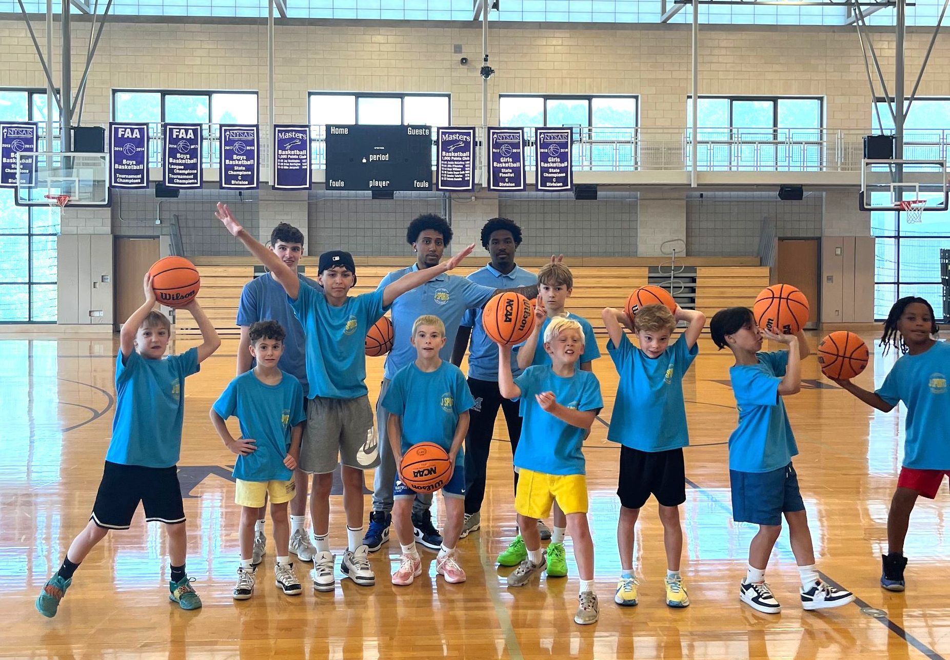 A group of children are standing on a basketball court holding basketballs.
