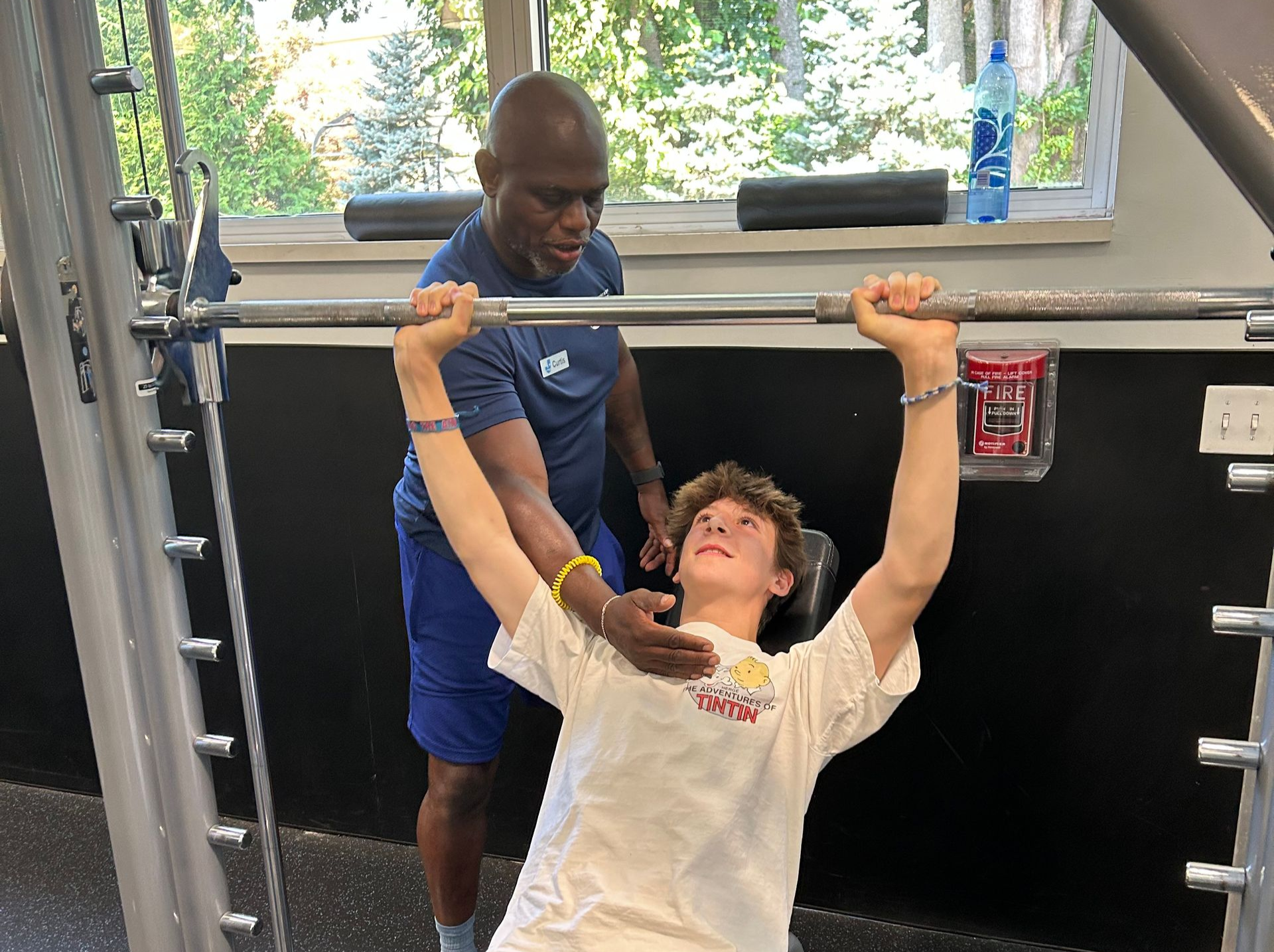 Man spotting a young person bench pressing in a gym.