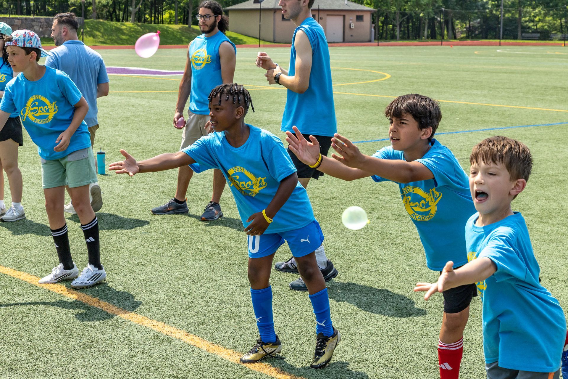 Children in blue shirts play catch with water balloons on a green field.