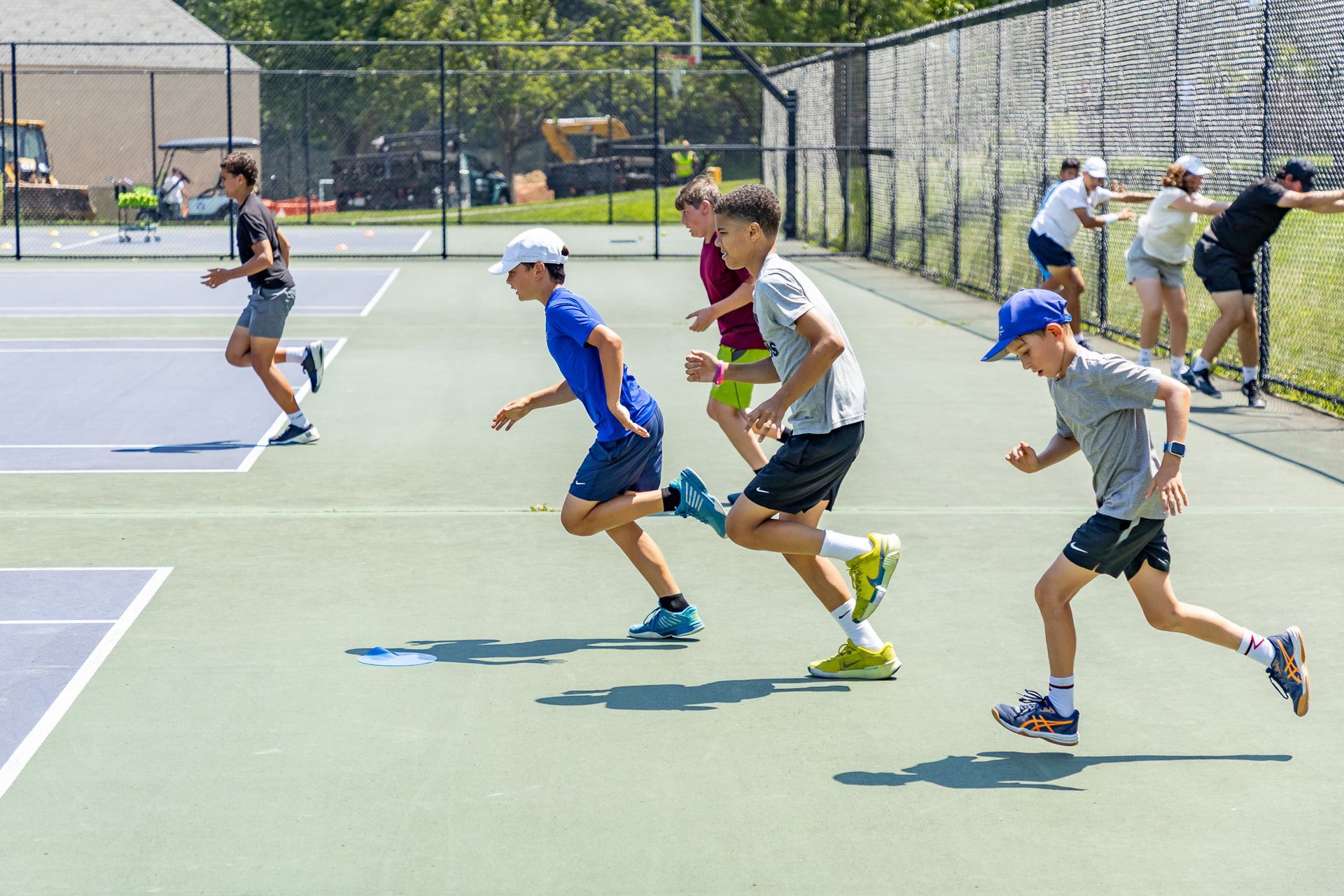Boys in athletic wear running on a tennis court, likely during training.