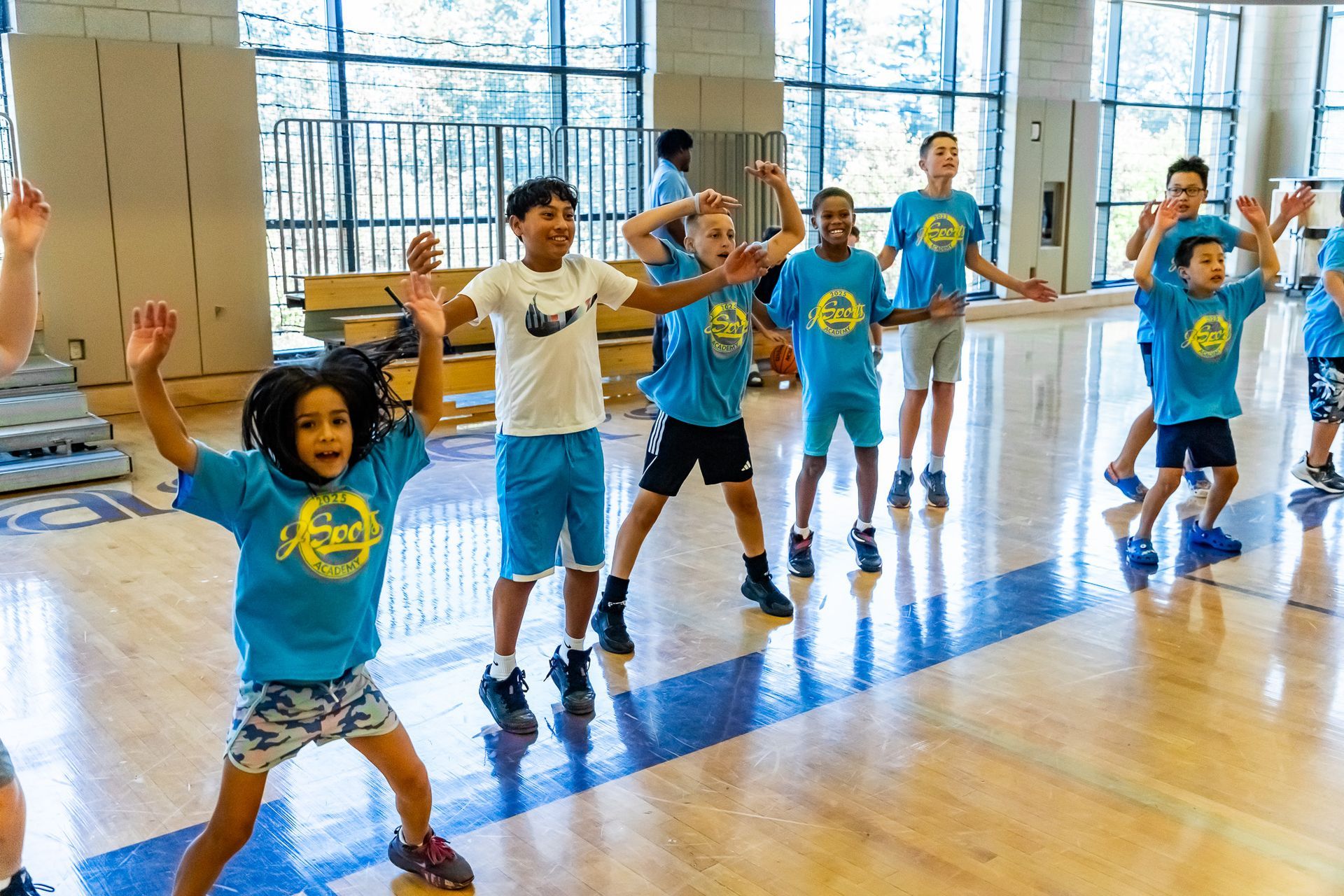 Kids in blue shirts exercising indoors, arms up, smiling.