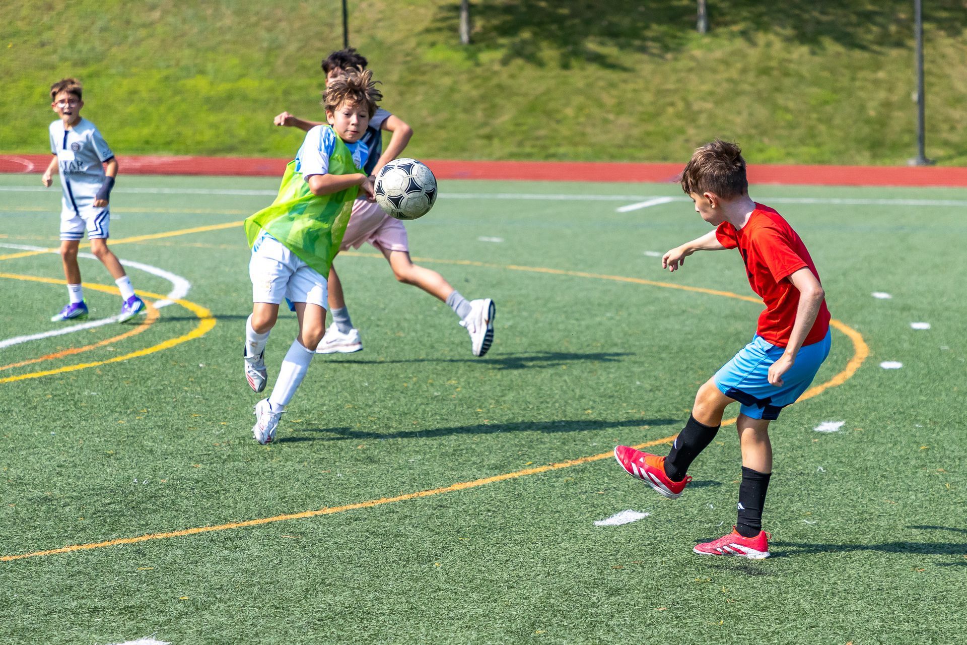 Boys playing soccer on a green field. One in red kicks, another in green tries to catch the ball.
