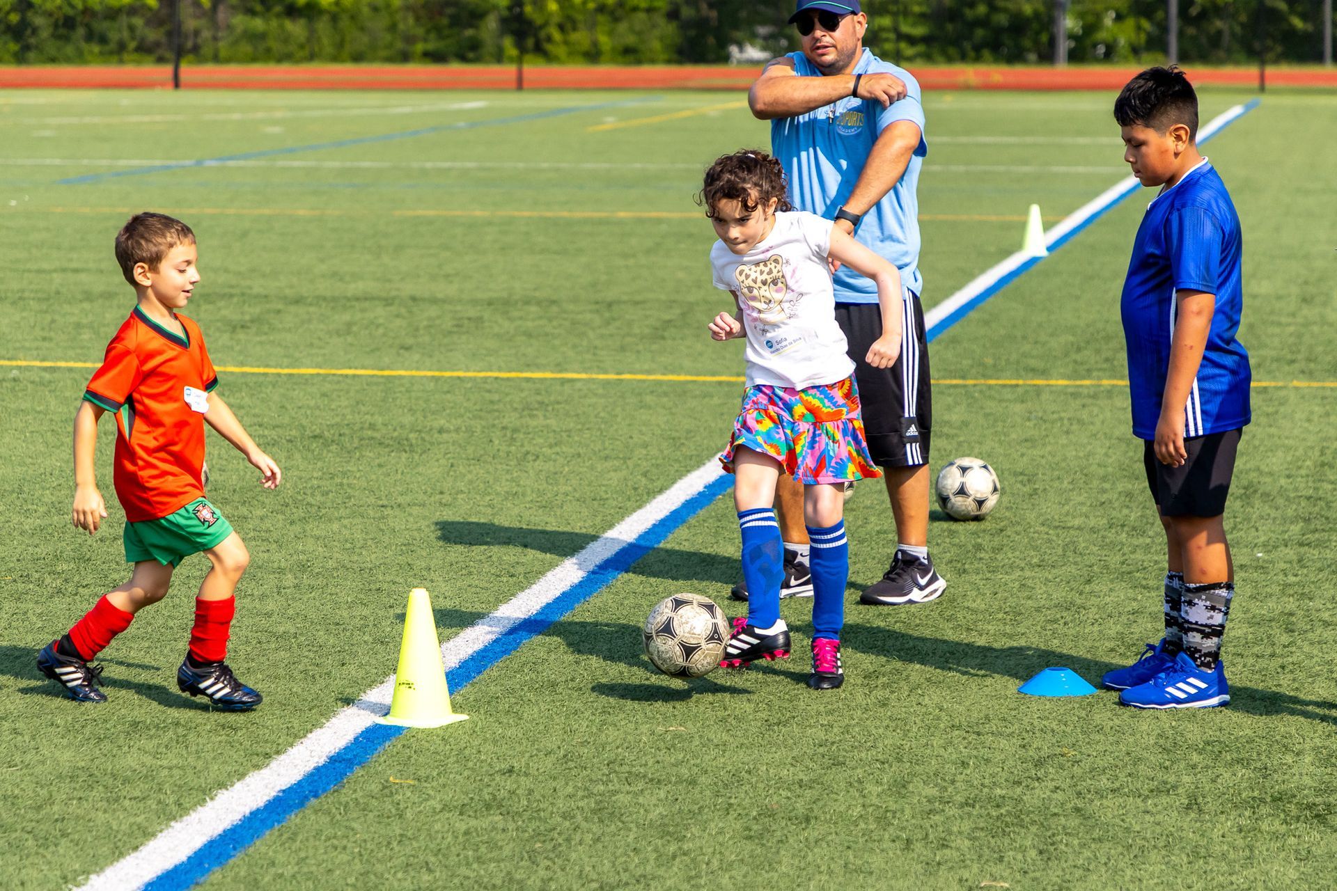 Children practicing soccer drills on a green field with a coach.