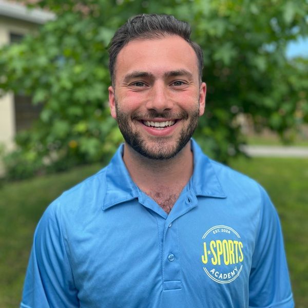 A man with a beard is wearing a blue polo shirt and smiling.