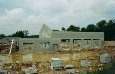 Construction site with gray cinder block walls and a partially built roof under a cloudy sky.