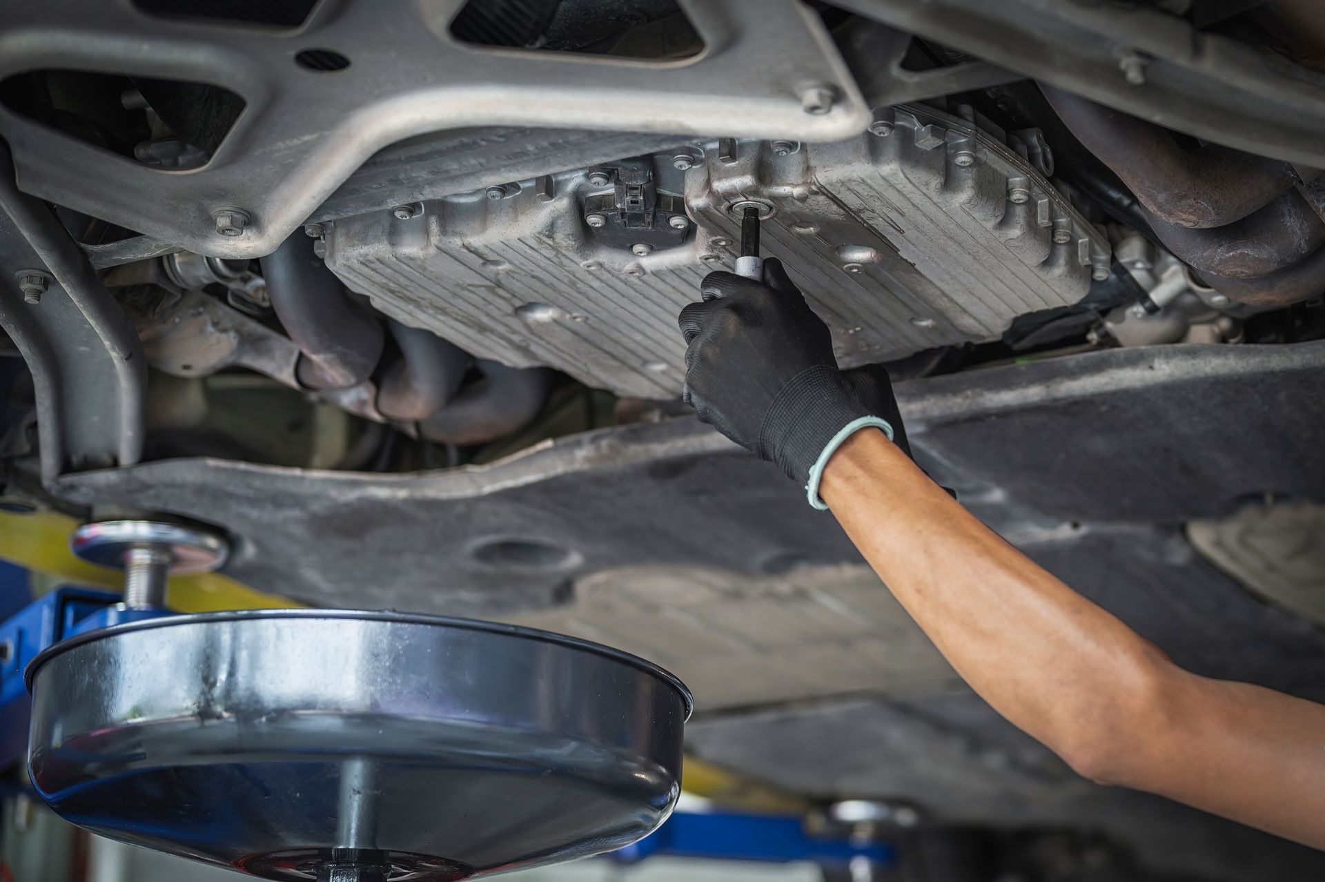 Mechanic draining car transmission fluid into a pan under a vehicle lift | Joe's Slinger Service, LLC