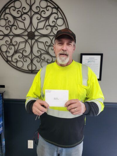 Man in high-vis shirt holding a card, standing in front of an ornamental wall decor and a framed document.