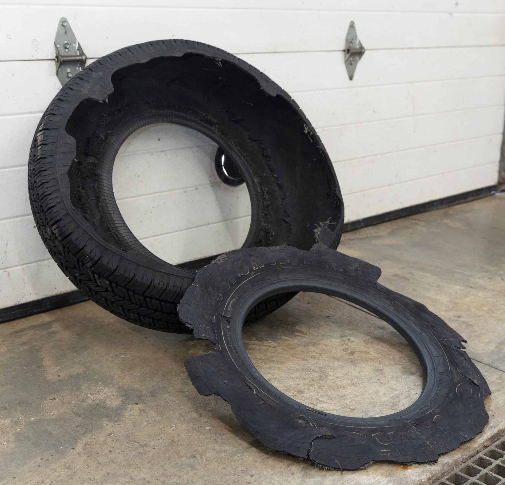 Damaged tire with a large chunk missing, on a concrete floor in front of a white garage door.