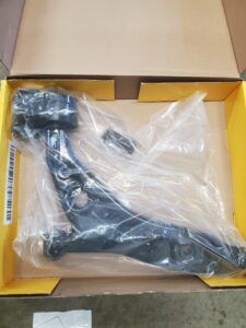 Black automotive control arm in a box, wrapped in plastic.