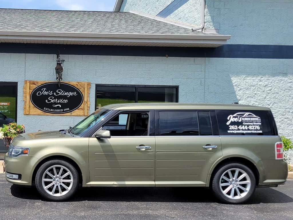 Gold Ford Flex parked outside a building with a sign for