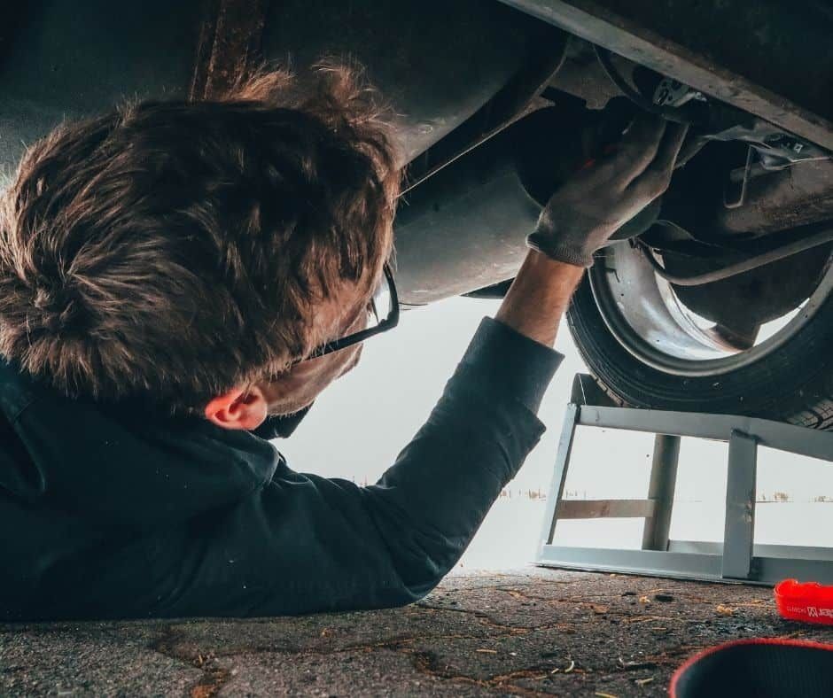 Mechanic working under a car, wearing gloves. Car is on a ramp.