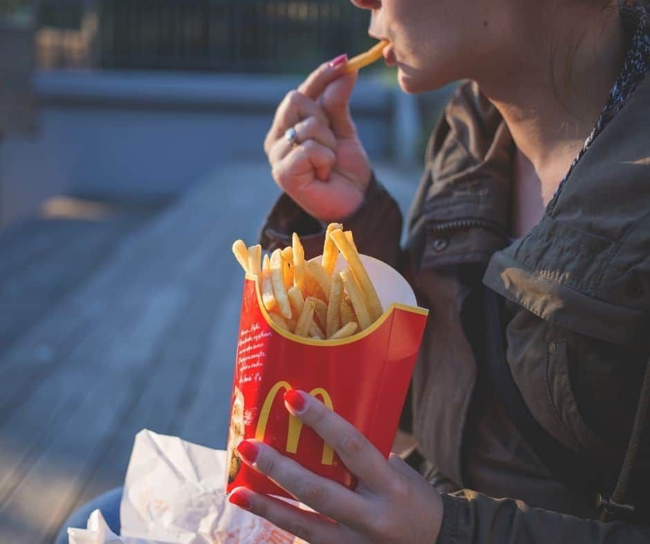 Person eating McDonald's french fries outdoors, red carton, wooden surface.