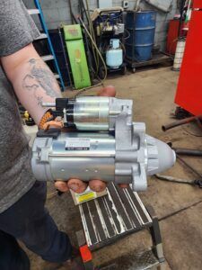 Person holding a new car starter in a repair shop.