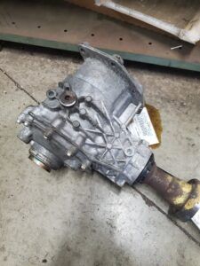 Silver differential with a rusty driveshaft, lying on concrete.