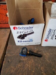 Boxes of Schrader EZ-sensor TPMS sensors. One sensor outside the box on a wooden surface.