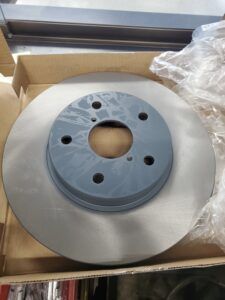 New car brake rotor, silver disc with a gray center, in a cardboard box.