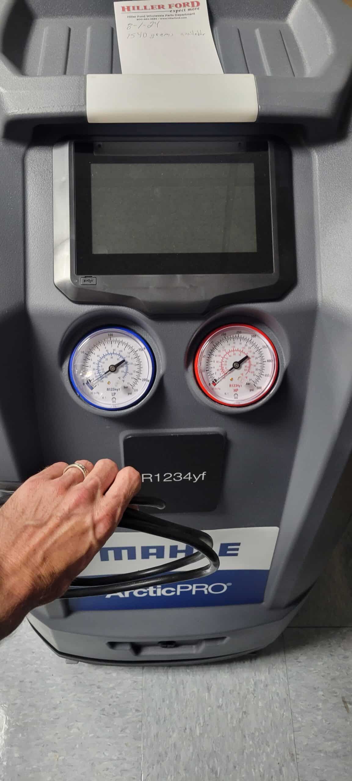 A/C machine with gauges, screen, and a handle, being held by a hand.