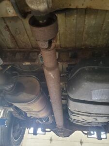 Undercarriage of a vehicle showing a rusted driveshaft, exhaust, and fuel tank.