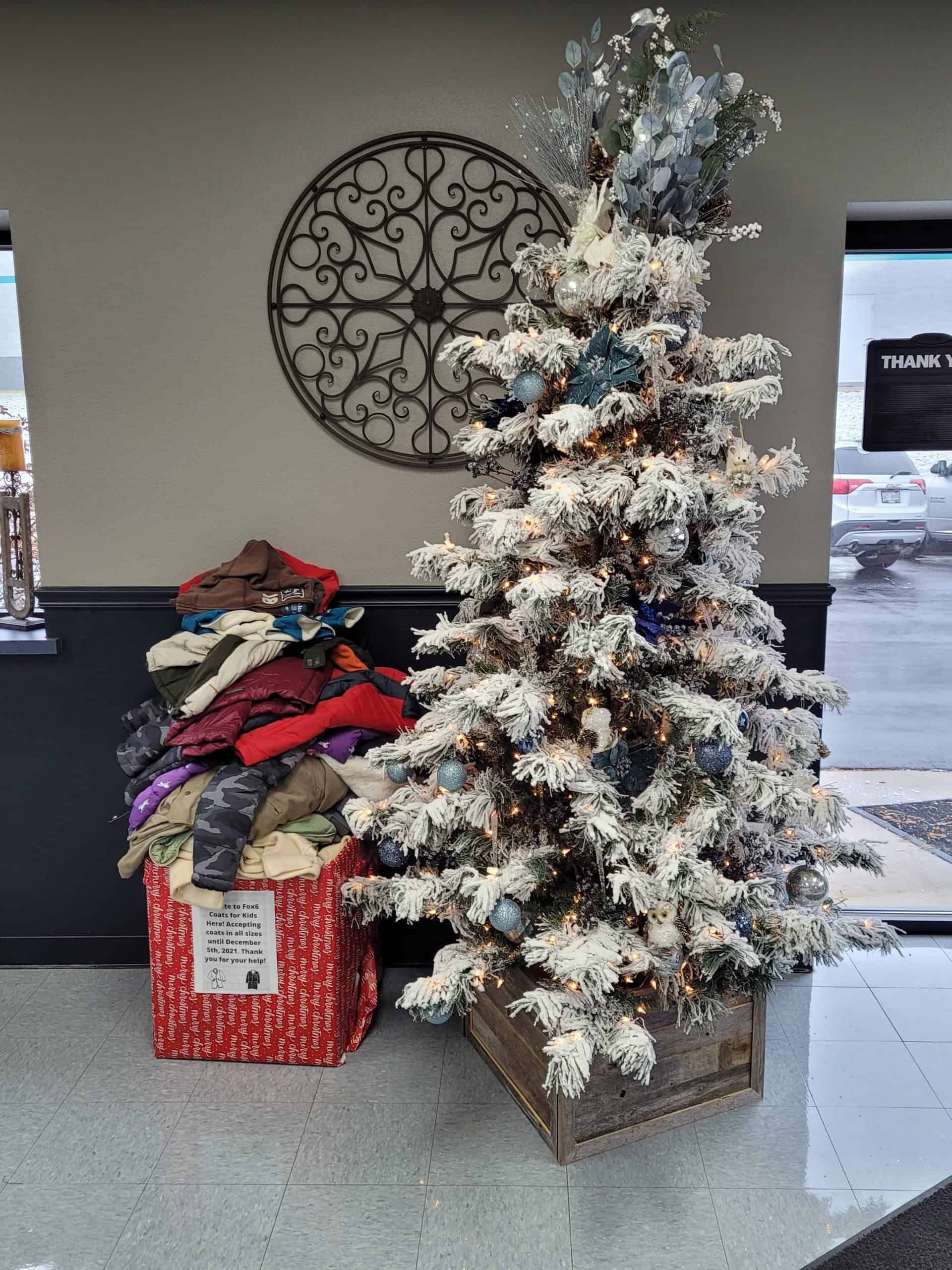 Christmas tree with snow-like effect and a donation box full of hats, next to a window.