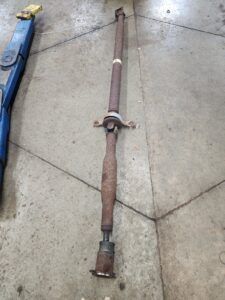 Rusty driveshaft on a concrete floor, with a blue lift in the background.