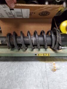 A car shock absorber and coil spring are on a workbench with a box in the background.